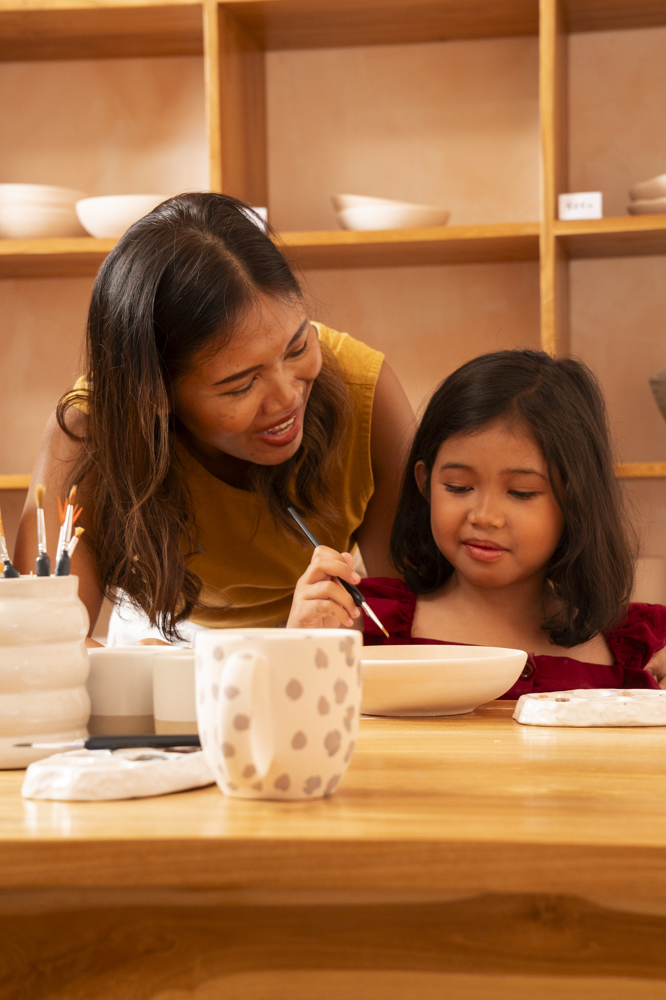 A parent guiding a child as they paint a ceramic bowl at Klay Bar in Canggu, capturing a quiet, shared moment of creativity in the studio.